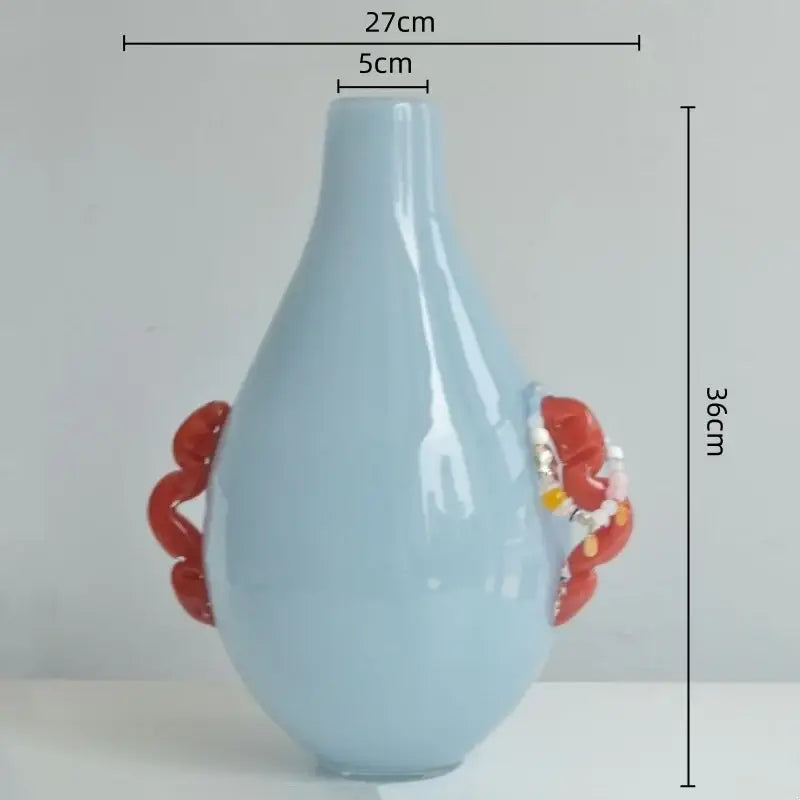 A light blue ceramic geometric flower vase with glossy finish and ornate red glass geometric handles for living room decor