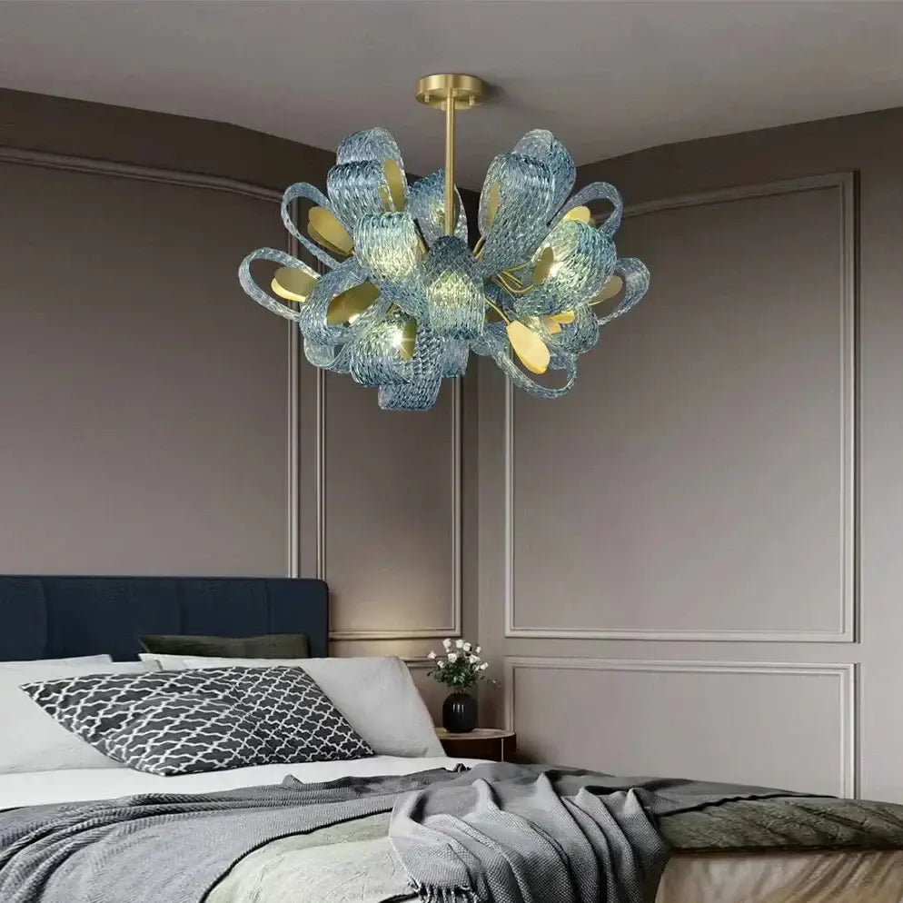 A modern blue peacock leaf glass chandelier with gold accents hangs above a bed as decorbites blue peacock decor