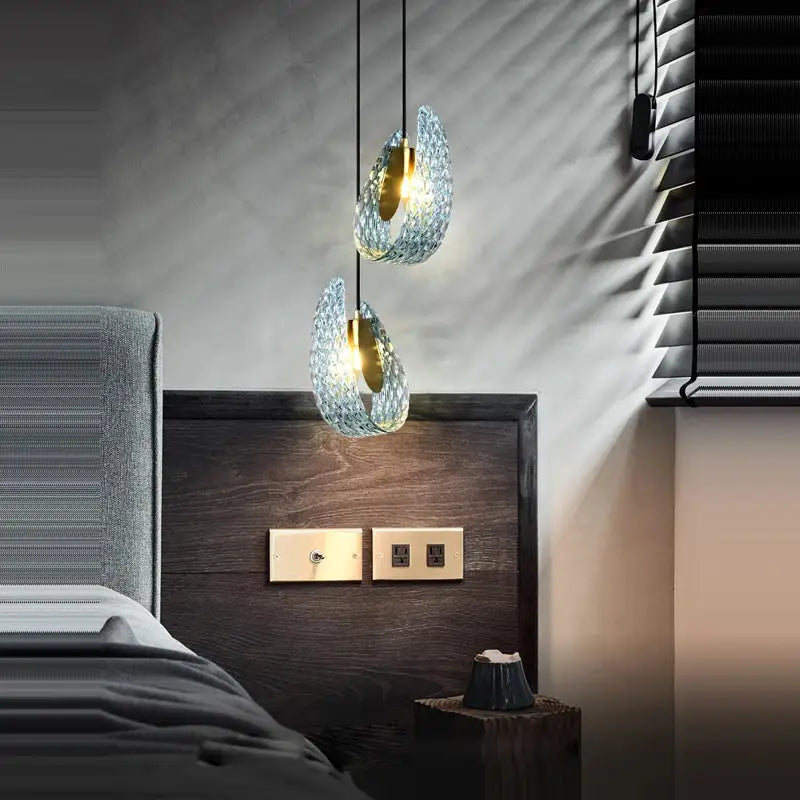 Two elegant blue queen crystal glass teardrop pendant lights with gold accents hang above a dark wood headboard