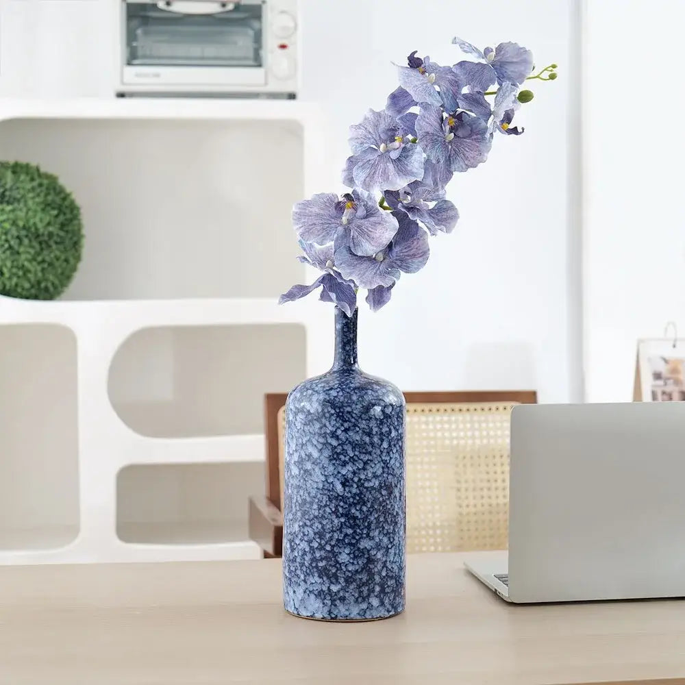 A tall blue ceramic vase with speckled porcelain finish holds purple orchids for modern living room decorbites decor