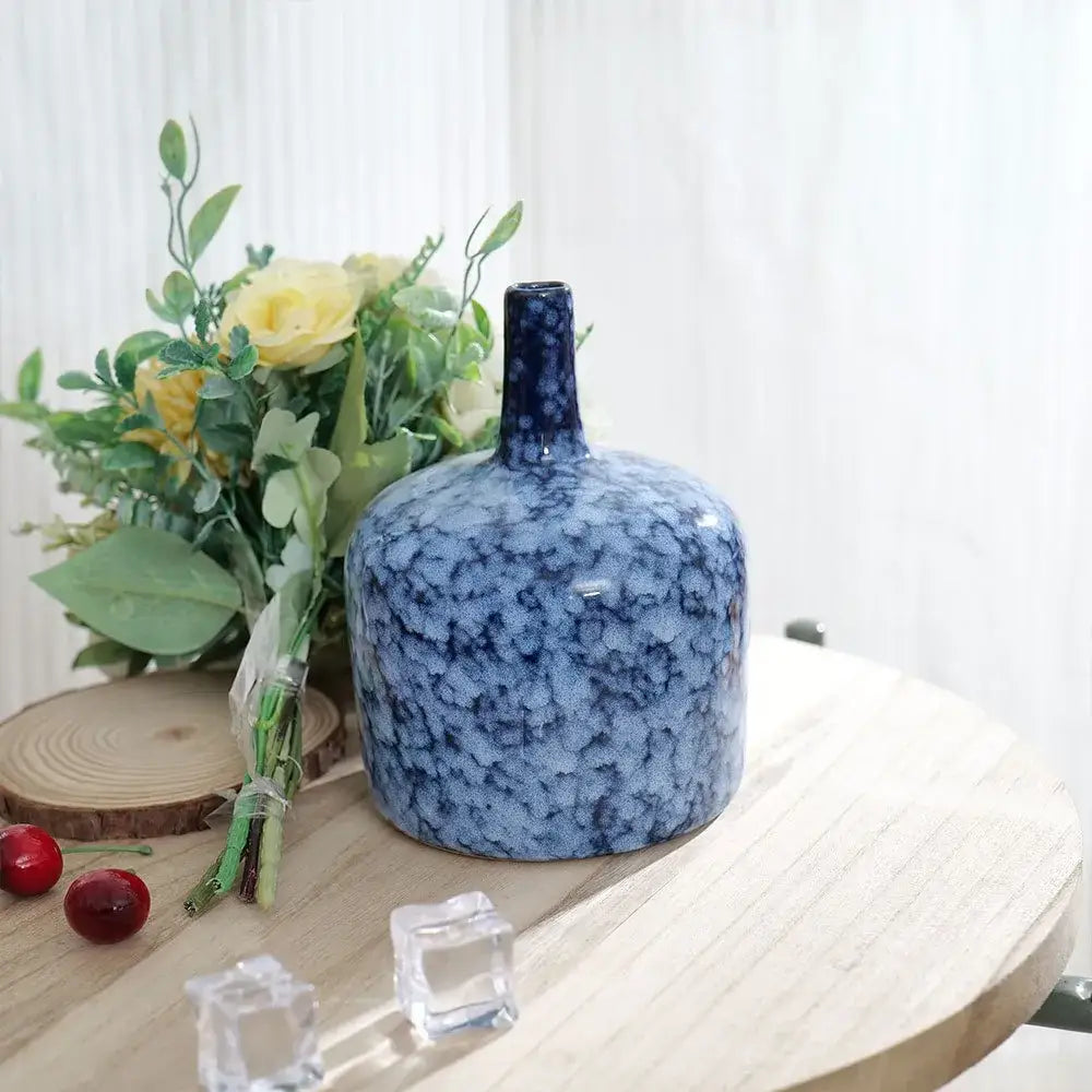 A modern blue ceramic vase with speckled porcelain glaze and slender neck on a wooden table for living room decorbites decor