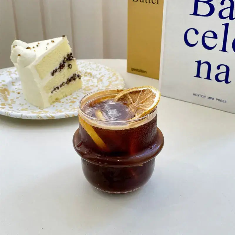 A modern borosilicate cap glass cup filled with dark iced coffee and garnished with a dried orange slice