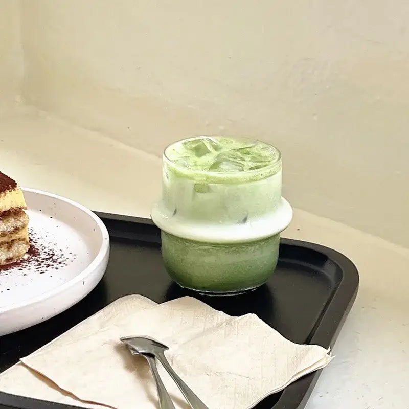 A layered green iced matcha drink in a clear modern borosilicate cap glass cup with ice and white rim for kitchen use