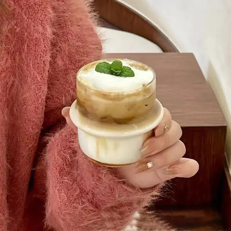 Modern borosilicate cap glass cup with layered iced coffee topped with whipped cream and fresh mint leaves in clear glass cup
