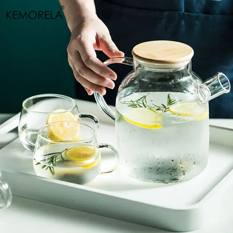 Modern borosilicate glass teapot with wooden lid and handle filled with infused water and lemon slices