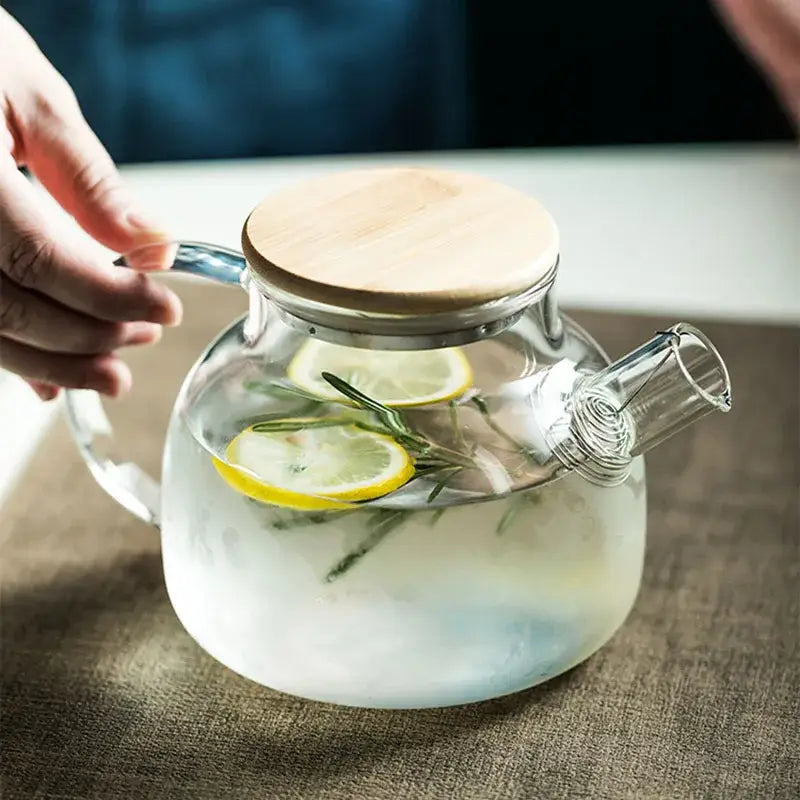Modern borosilicate glass teapot with light wood handle filled with lemon slices and rosemary in transparent borosilicate glass