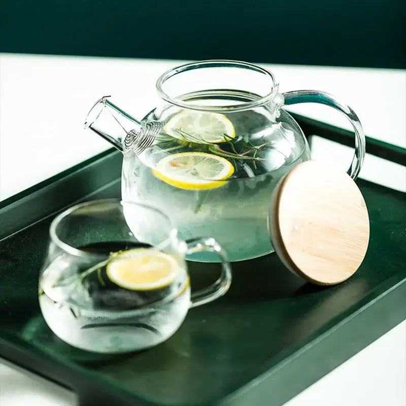 Modern borosilicate glass teapot with wooden lid and handle filled with lemon slices and rosemary sprigs in transparent borosilicate glass