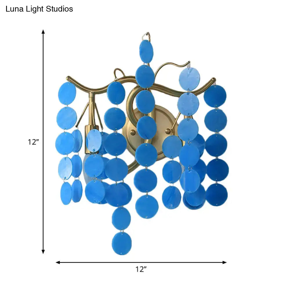 Blue circular glass discs hang from a brass wall lamp with a modern branch design for bedroom sconce use