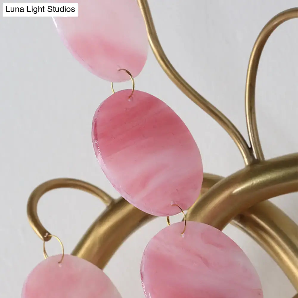 Pink oval-shaped resin earrings with marbled finish and gold-toned hooks next to modern branch design blue and pink glass wall lamp bedroom sconce