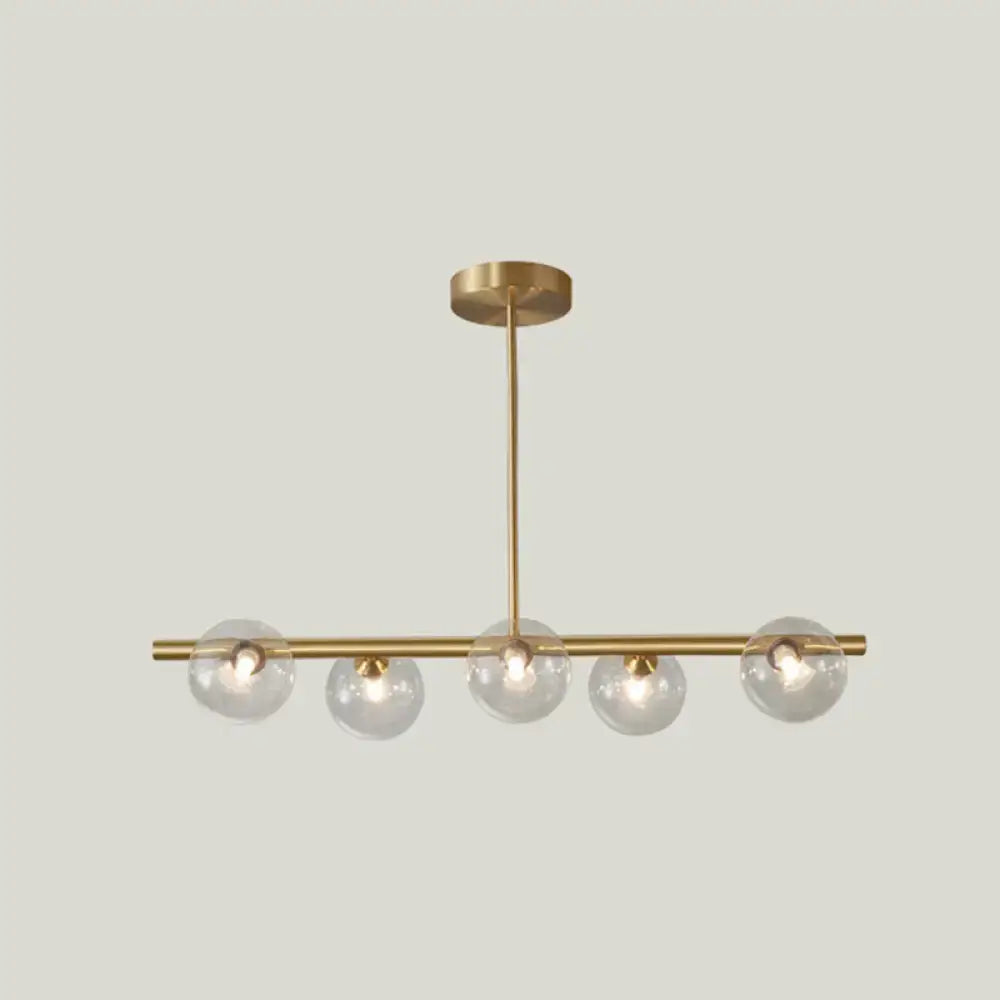 Modern brass pendant light with five clear spherical glass shades designed for dining room illumination