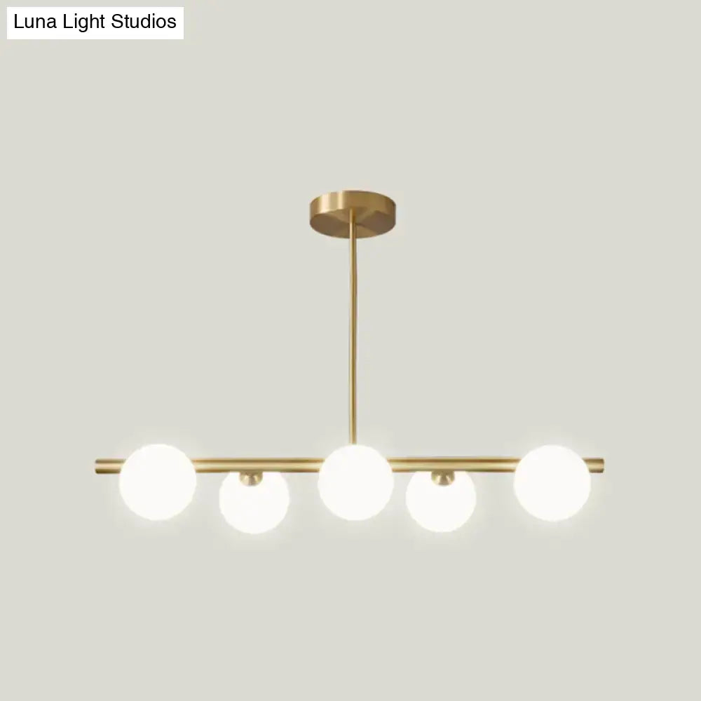 Modern brass pendant light with five spherical glass shade bulbs in a linear design for dining room lighting