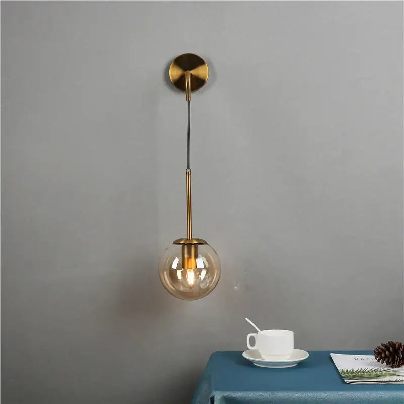 A modern brass wall lamp with a spherical amber decorbites glass ball housing an exposed bulb for bedroom light