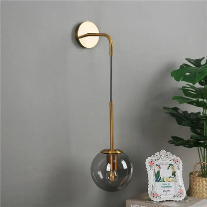 Modern brass amber glass ball wall lamp with gold-toned curved arm and smoked glass shade for bedroom decorbites glass ball