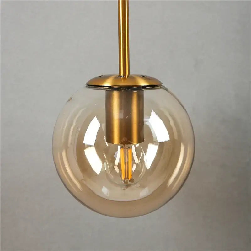 Modern brass amber glass ball wall lamps featuring a clear glass globe with gold-toned metal and exposed filament bulb