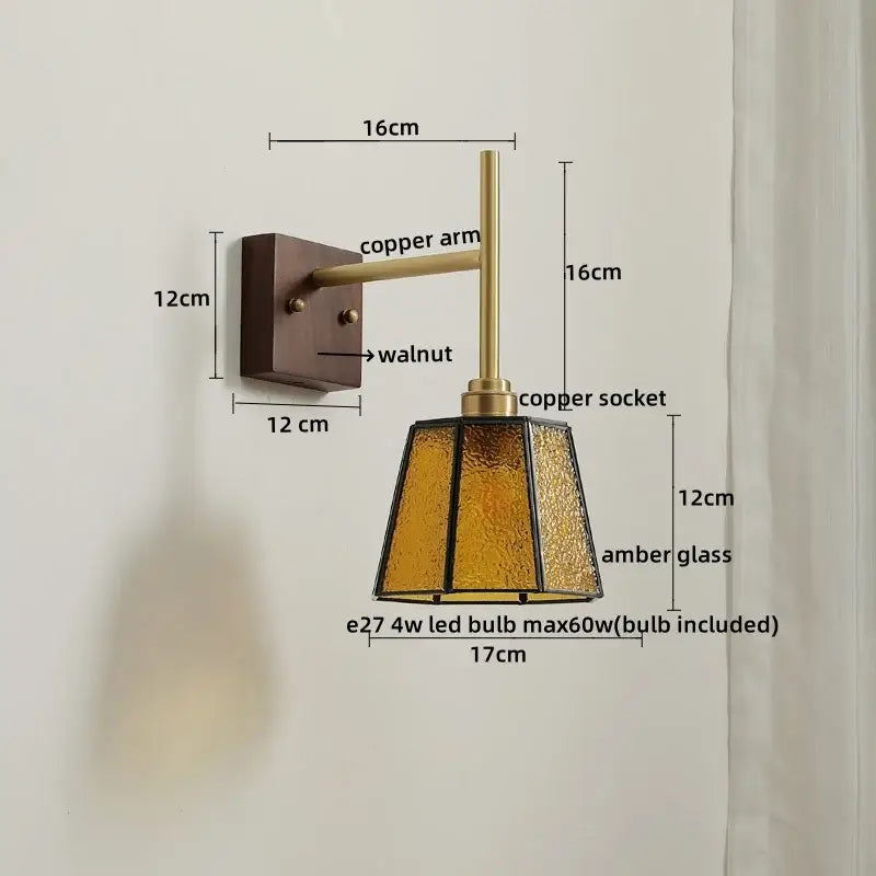 A warm amber glass copper led wall light with textured faceted design and copper hardware on walnut wall plate