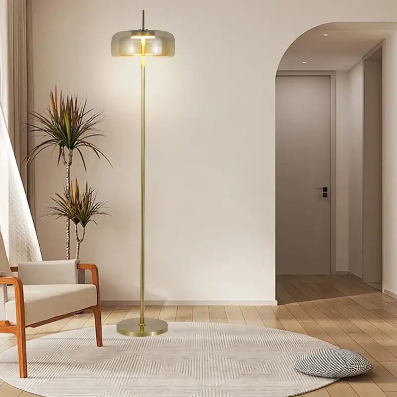 Modern brass and amber glass led floor lamp with cylindrical glass shade emitting warm light for living room lighting