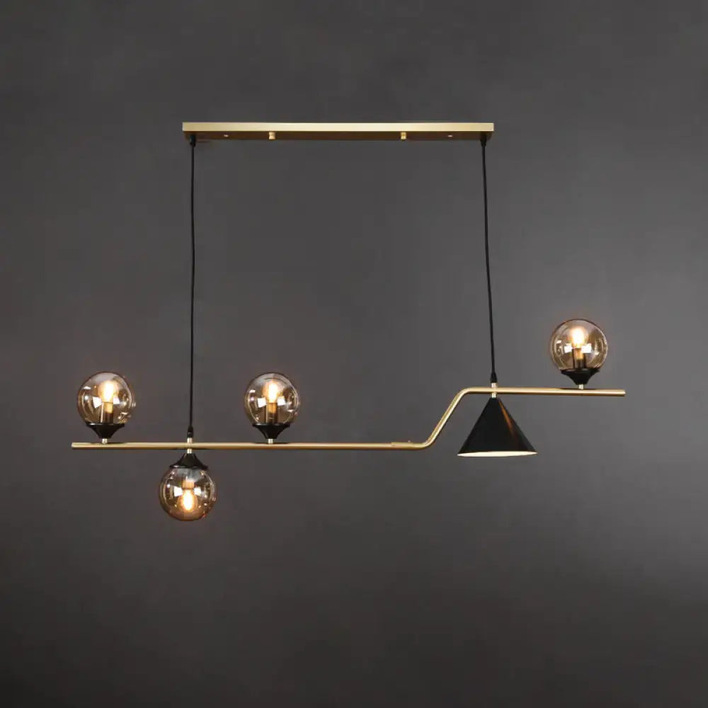 Modern brass pendant light with three amber glass ball hanging bulbs and one black conical shade for dining island