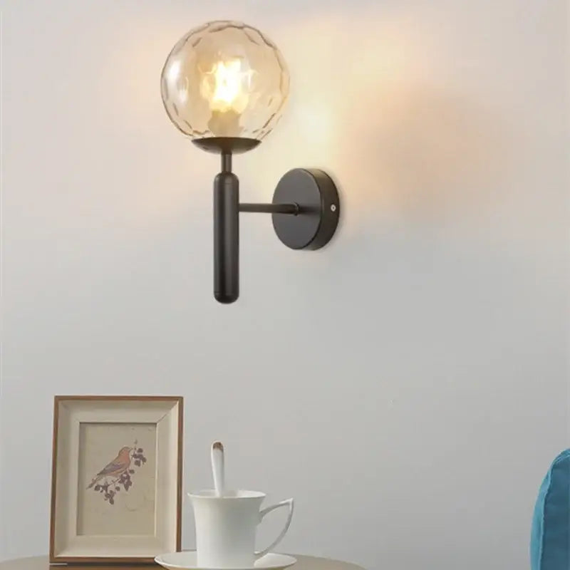 A warm-toned art glass ball sconce with black art glass and matte black metal arm for modern living room lighting
