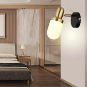 Modern brass and black glass sconce light with frosted glass shade and circular base for bedroom wall lighting