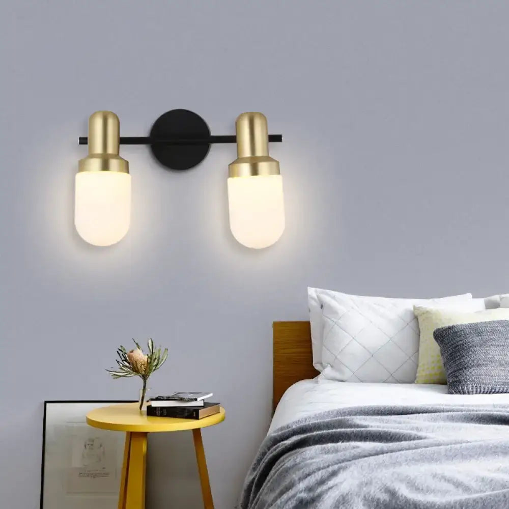 Modern brass and black glass sconce light with frosted glass shades and black circular mounting plate for bedroom wall