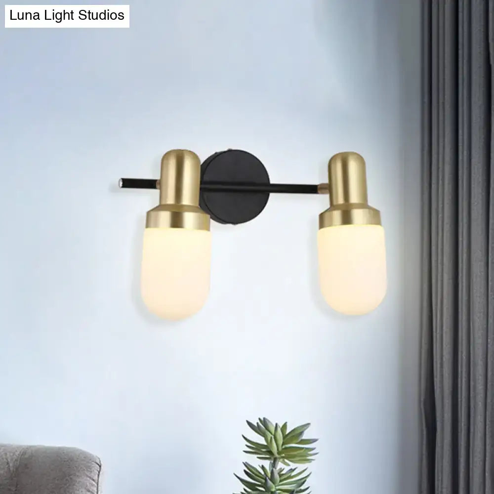 Modern brass and black glass sconce light with two brushed brass cylindrical shades and black circular mount for bedroom wall