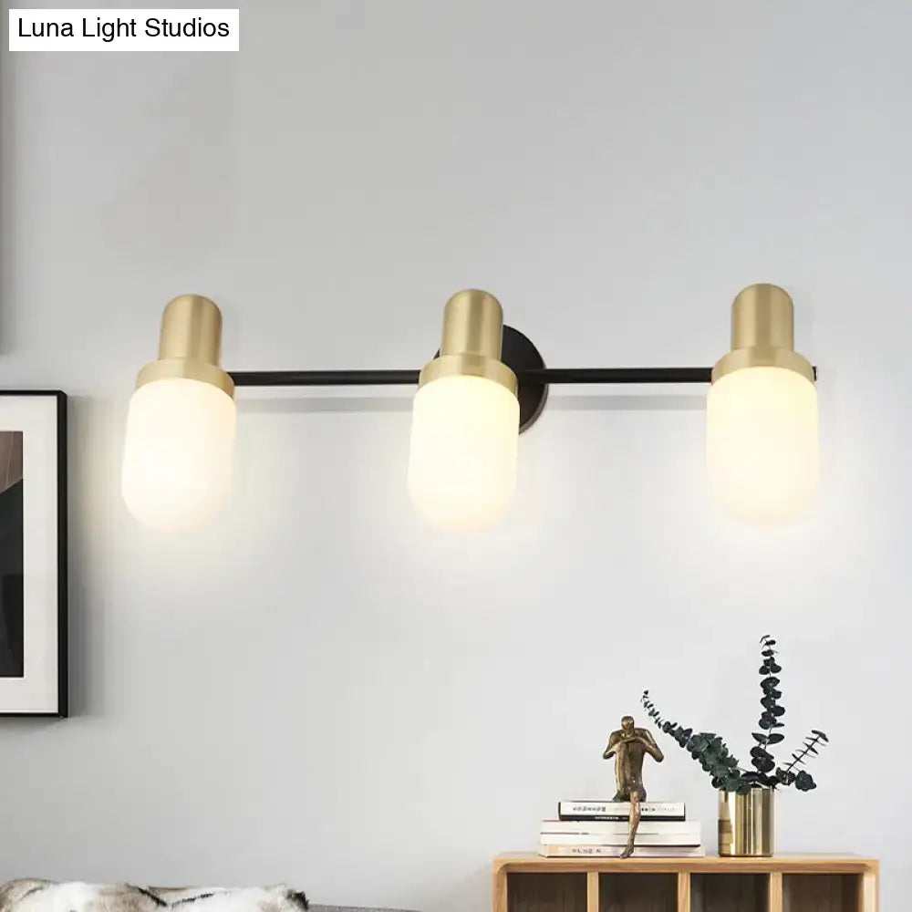 Modern brass and black glass sconce light with brushed gold cylindrical fixtures and frosted glass shades for bedroom wall use