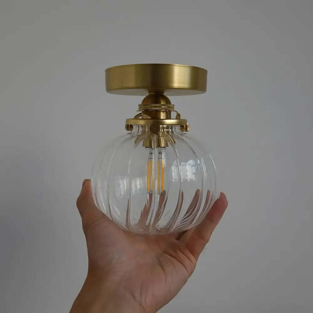 Modern brass wall sconce with clear ribbed glass ball and exposed led filament bulb for bedroom use