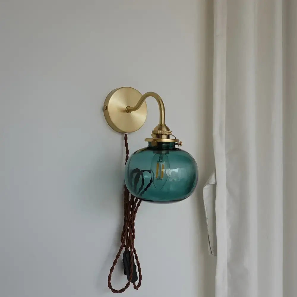 Modern brass and blue glass ball wall sconce with teal glass globe, brass hardware, and braided cord for bedroom use