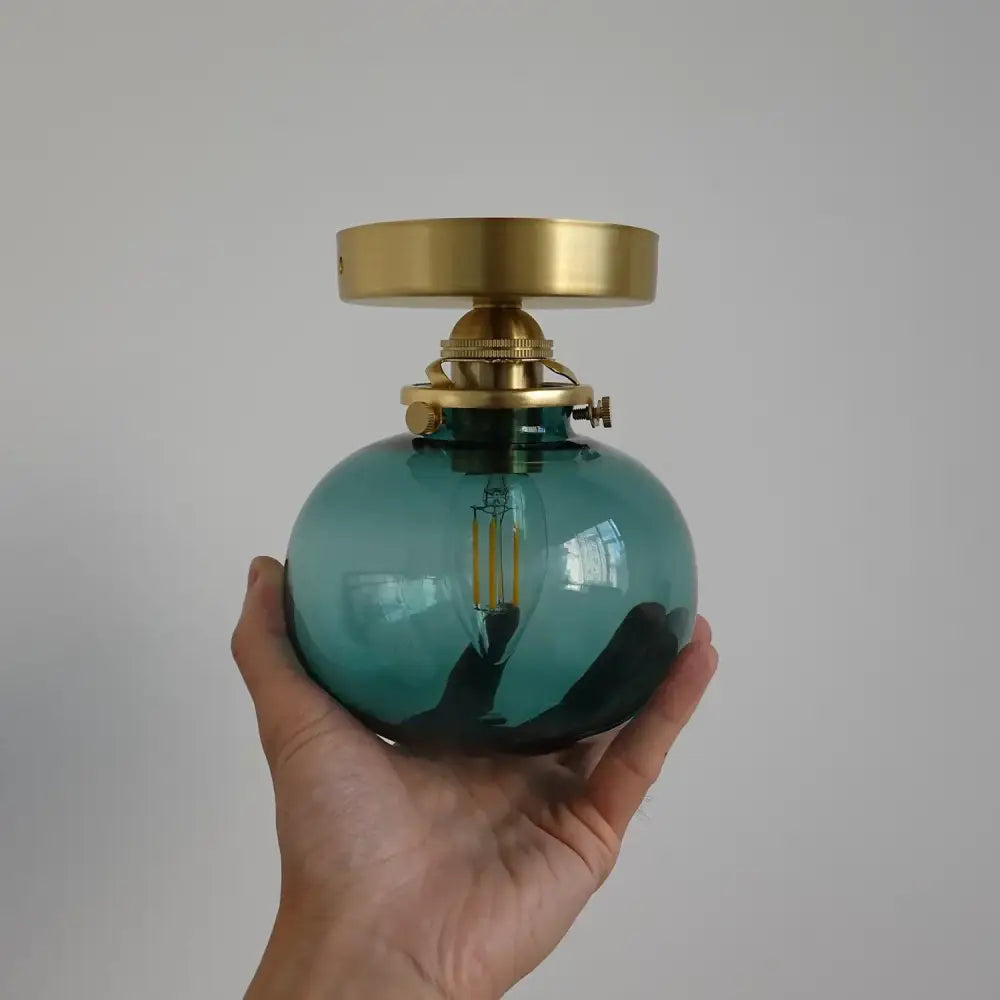 Modern brass and blue glass ball wall sconce with pull chain featuring a teal glass ball and brass-finished metal fittings