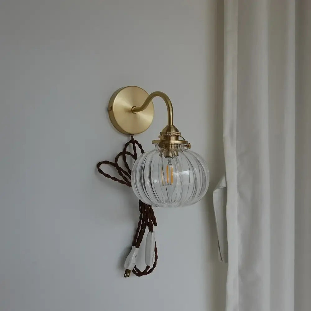 Modern brass wall sconce with clear ribbed glass ball and brass-finished arm ideal for bedroom lighting