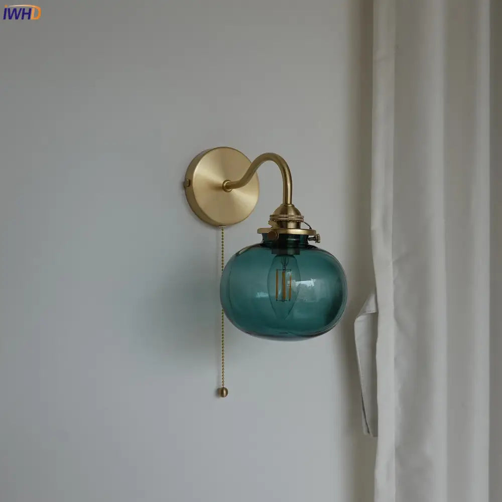 Modern brass and blue glass ball wall sconce featuring a teal glass ball with exposed filament bulb and pull chain switch