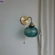 Modern brass and blue glass ball wall sconce featuring a teal glass ball with exposed filament bulb and pull chain switch