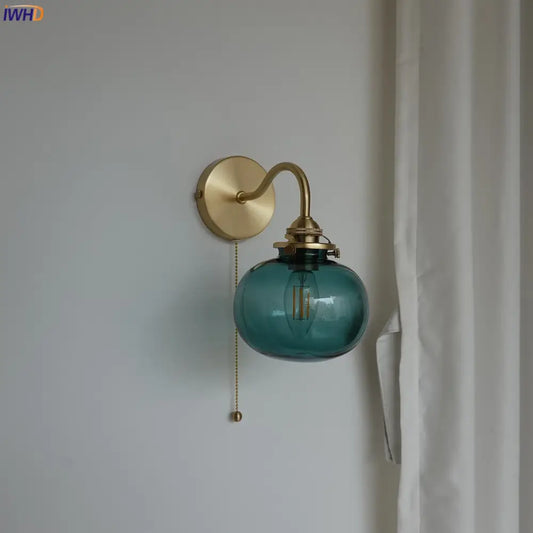 Modern brass and blue glass ball wall sconce featuring a teal glass ball with exposed filament bulb and pull chain switch