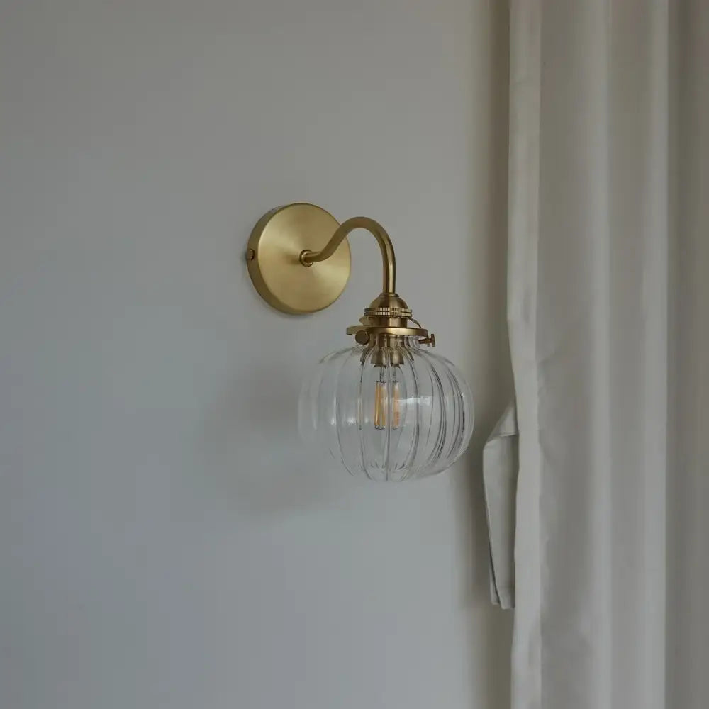 Modern brass wall sconce with a blue glass ball and clear ribbed globe housing an exposed filament bulb for bedroom use