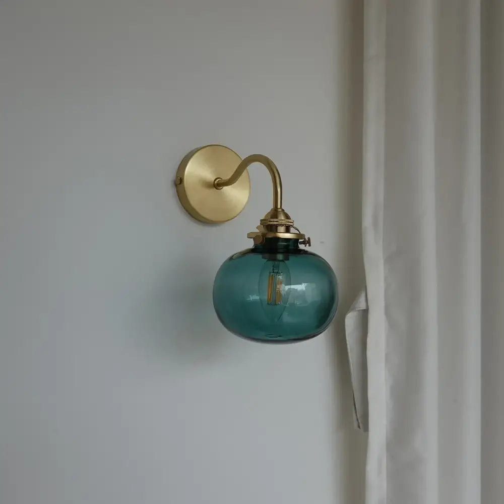 Modern brass and blue glass ball wall sconce with teal glass globe and pull chain for bedroom lighting