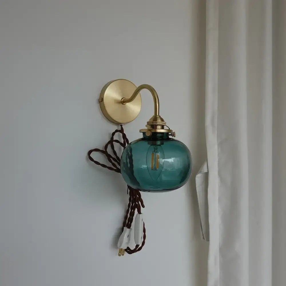 Modern brass and blue glass ball wall sconce with teal glass ball, brass hardware, and braided brown cord for bedroom use