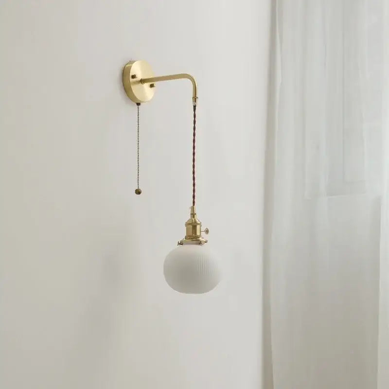 Modern brass and ceramic copper led wall lamp with off-white spherical glass shade and brass-finished metal arm decorbites ceramic copper