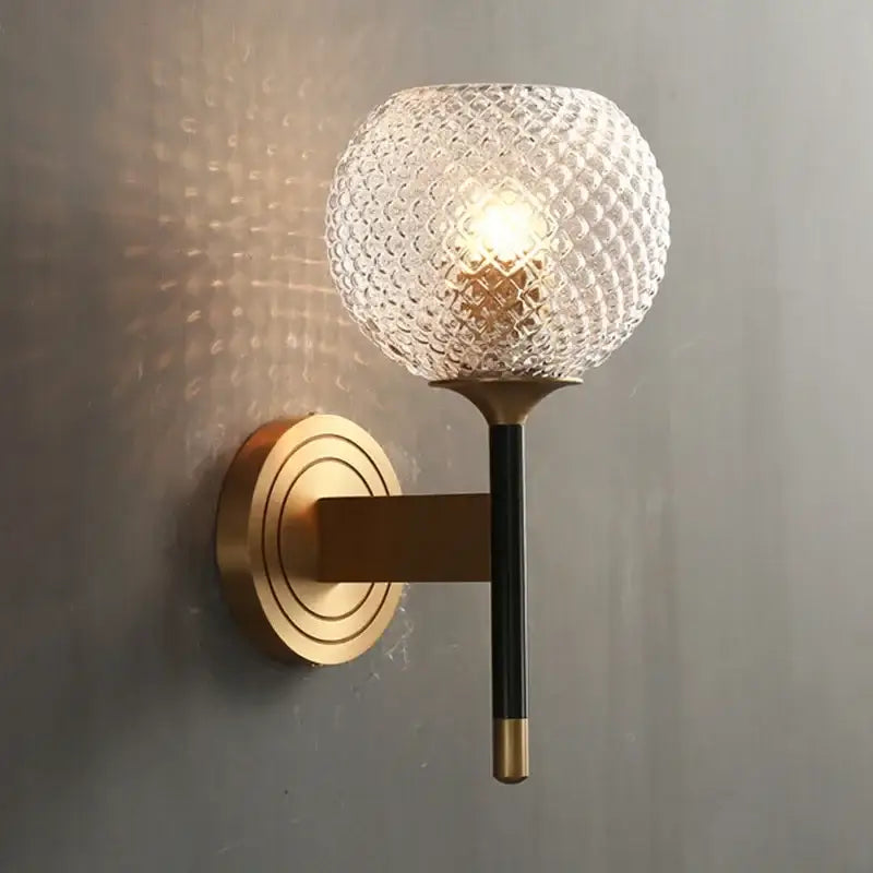 A modern wall light with a textured clear glass globe and brass accents in a decorbites copper wooden frame
