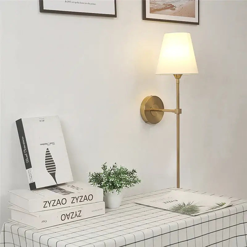 Modern brass and cream fabric led wall lamps feature a gold-toned wall sconce with tapered off-white fabric shade for bedroom use