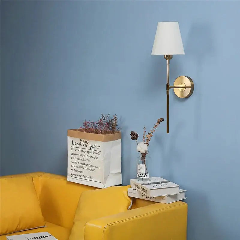 Modern brass and cream fabric led wall lamps featuring a gold-toned wall sconce with white conical shade for bedroom use