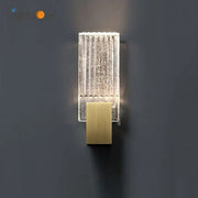 Modern brass and crystal wall light featuring a clear textured glass sconce with vertical ridges and illuminated interior