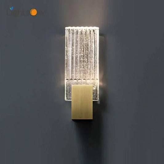 Modern brass and crystal wall light featuring a clear textured glass sconce with vertical ridges and illuminated interior