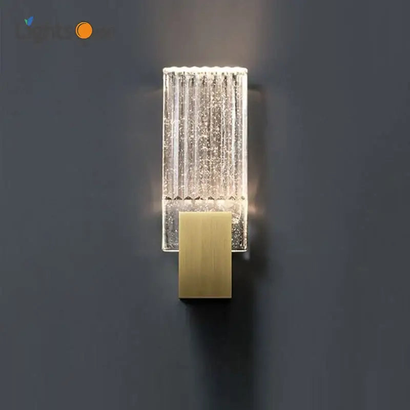 Modern brass and crystal wall light featuring a clear textured glass sconce with vertical ridges and illuminated interior
