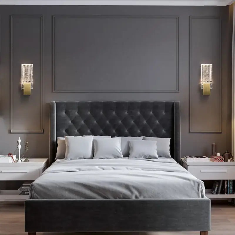 Modern brass and crystal wall light glass sconce illuminating dark gray tufted velvet headboard and matching footboard