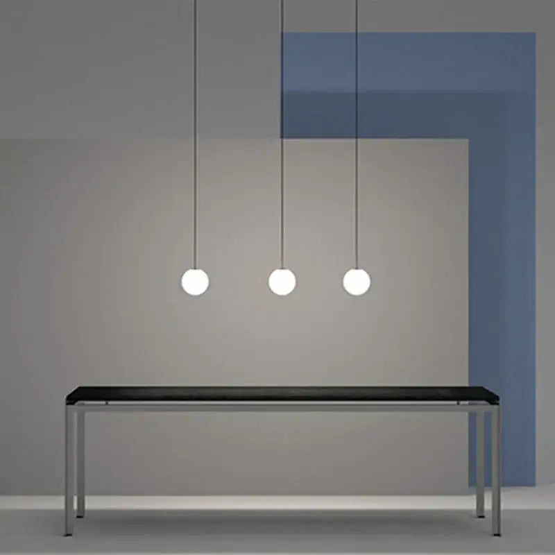 Three minimalist white frosted glass ball pendant lights hang above a sleek black tabletop modern pendant light decorbites glass ball