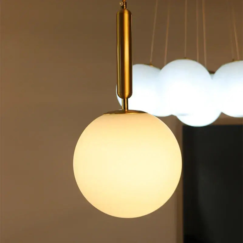 Modern brass and frosted glass pendant light with warm-toned spherical glass and polished brass stem chandelier pendant light