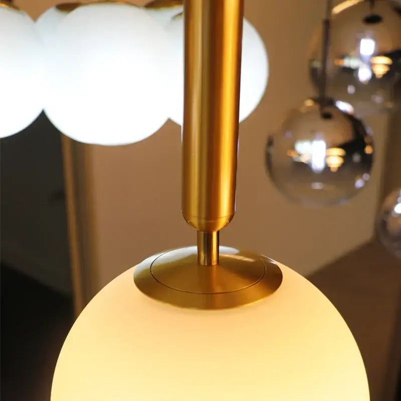 Modern brass and frosted glass pendant light with golden metallic stem and glowing opaque white spherical lampshade
