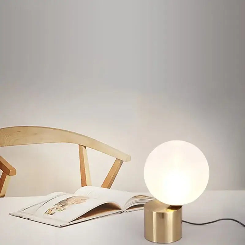 A modern brass and glass ball table lamp with a frosted globe and brushed brass base ideal for bedroom decorbites