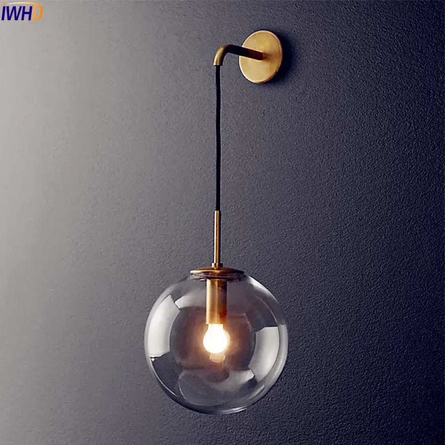 A sleek modern brass and glass ball wall lamp with a clear globe and black cord for bathroom decorbites glass ball