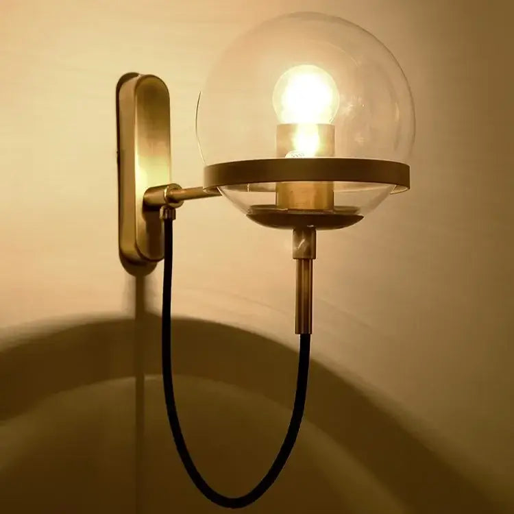 Modern brass and glass globe led wall lamps featuring a brass-finished sconce with clear globe and black cord wall lamps